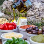 Outdoor picnic with various Mediterranean spreads, herbs, and olive oil drizzle.