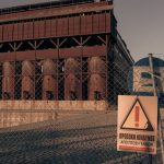 Rusty industrial building with warning sign and fence under warm sunlight.